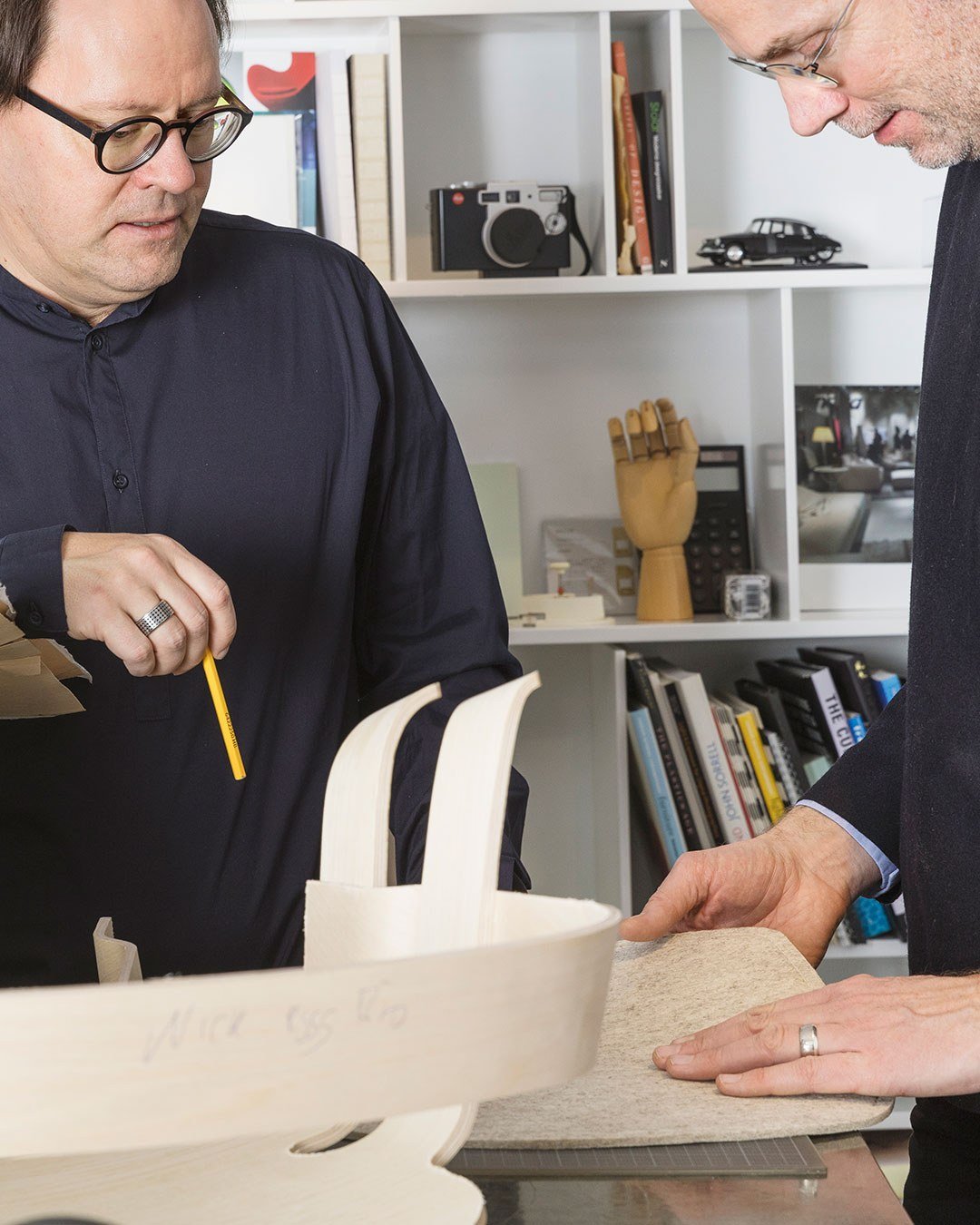Two designers marking a moulded wooden chair shell with a pencil.