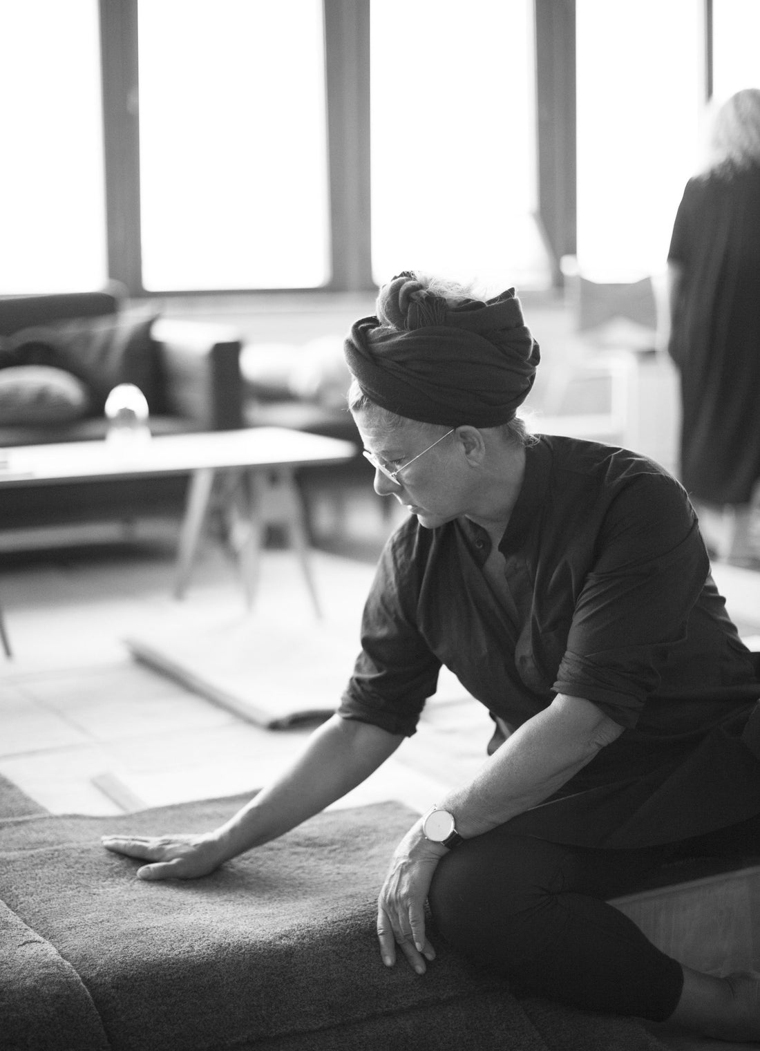 A designer kneeling to run her hand across a rug in the studio.
