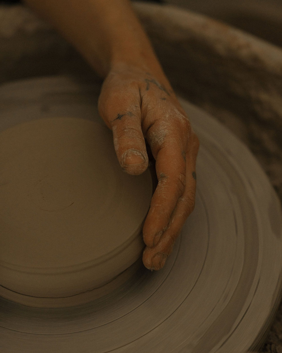 A clay-covered hand shapes a piece of clay on the turning potter's wheel.