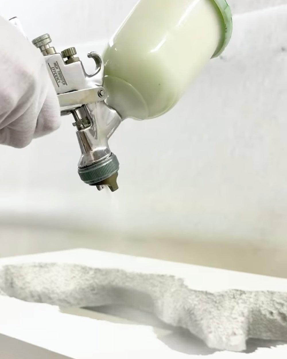 A gloved hand sprays a coating onto a carved foam surface at Gufram