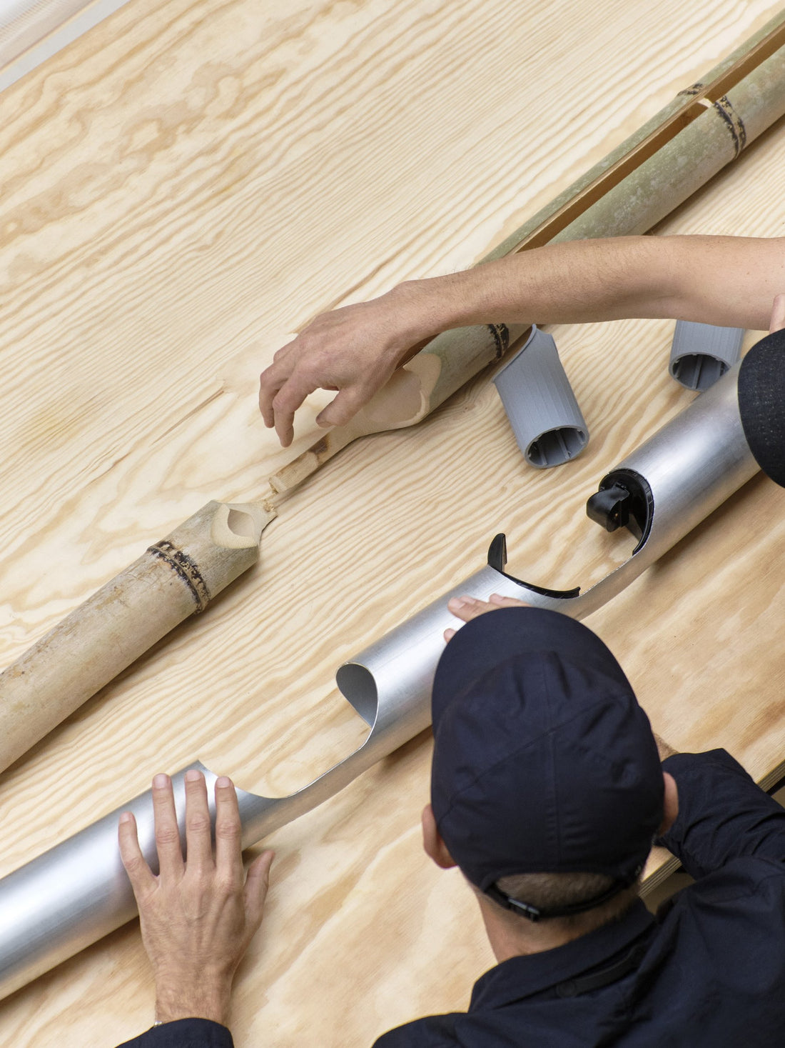 Seen from above, hands arranging aluminium tubes and joints on a wooden tabletop while developing a table.