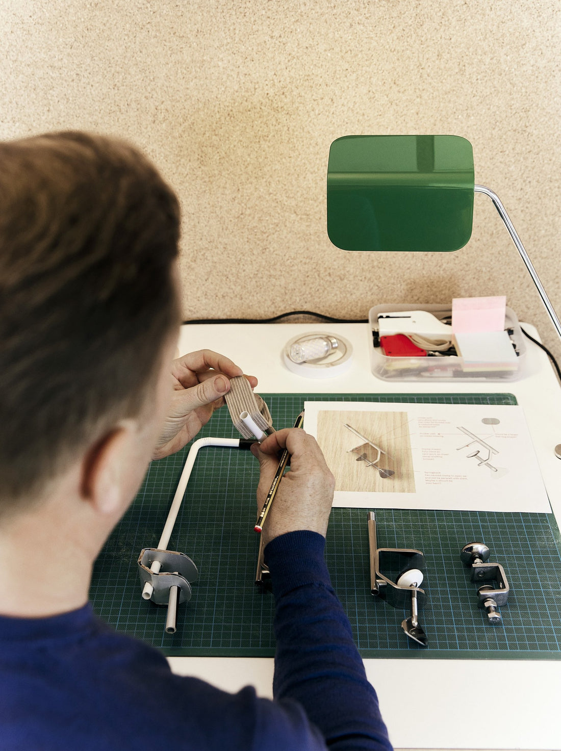 A designer assembling the joint of a desk lamp prototype on a green cutting mat.