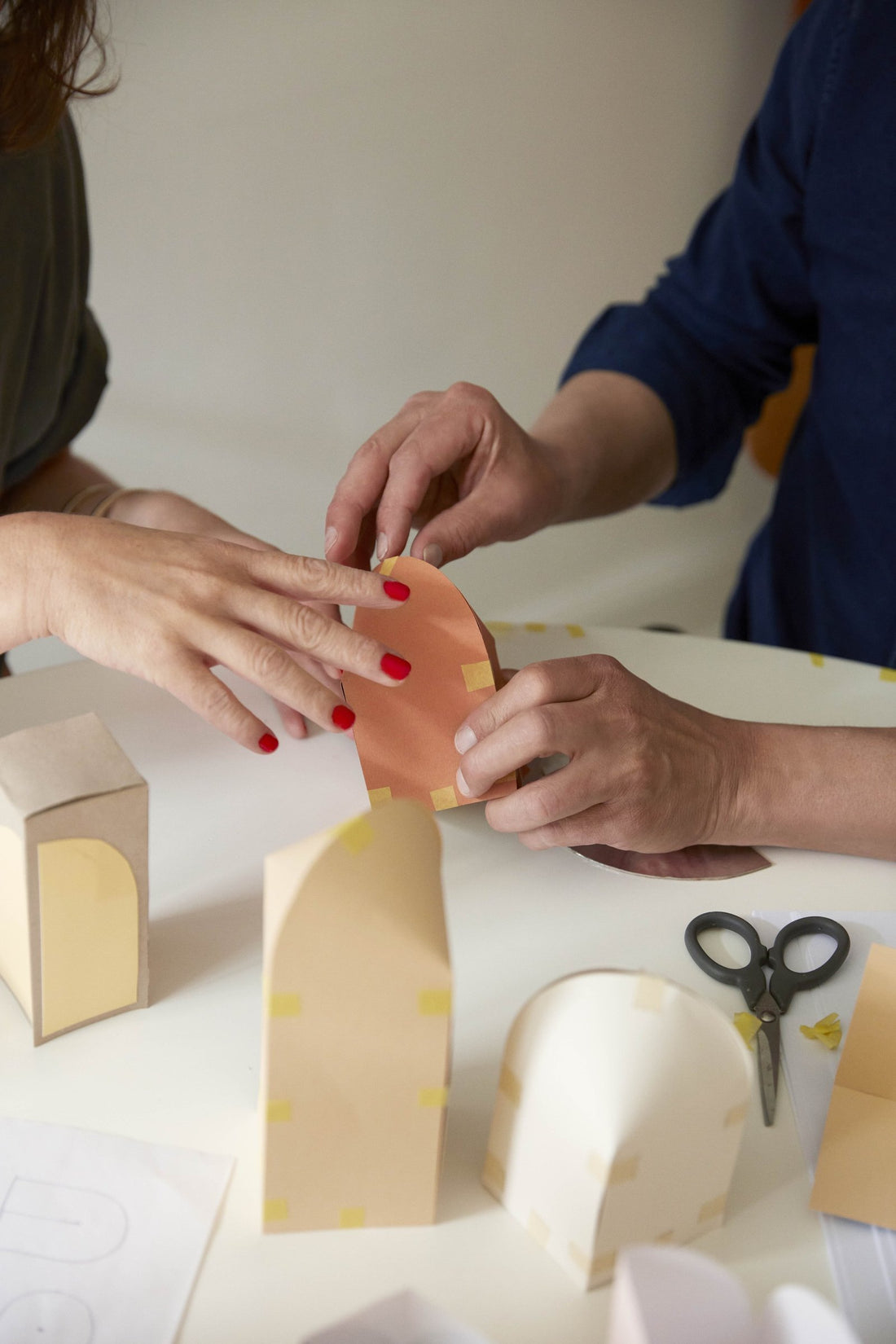 Two pairs of hands shaping paper models of a lamp shade in the studio.