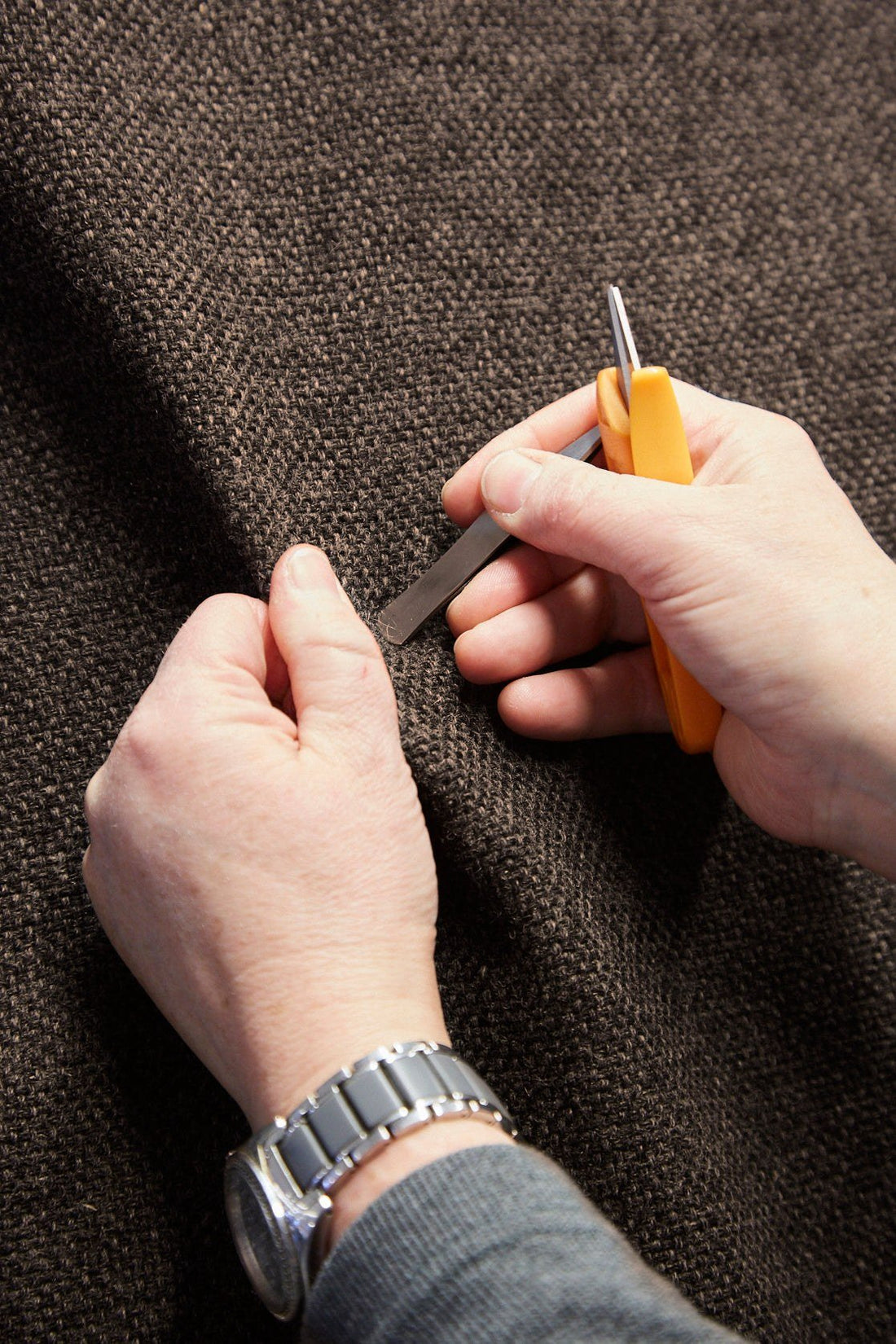Hands inspecting a woven wool fabric with a small tool at a Norwegian textile mill.