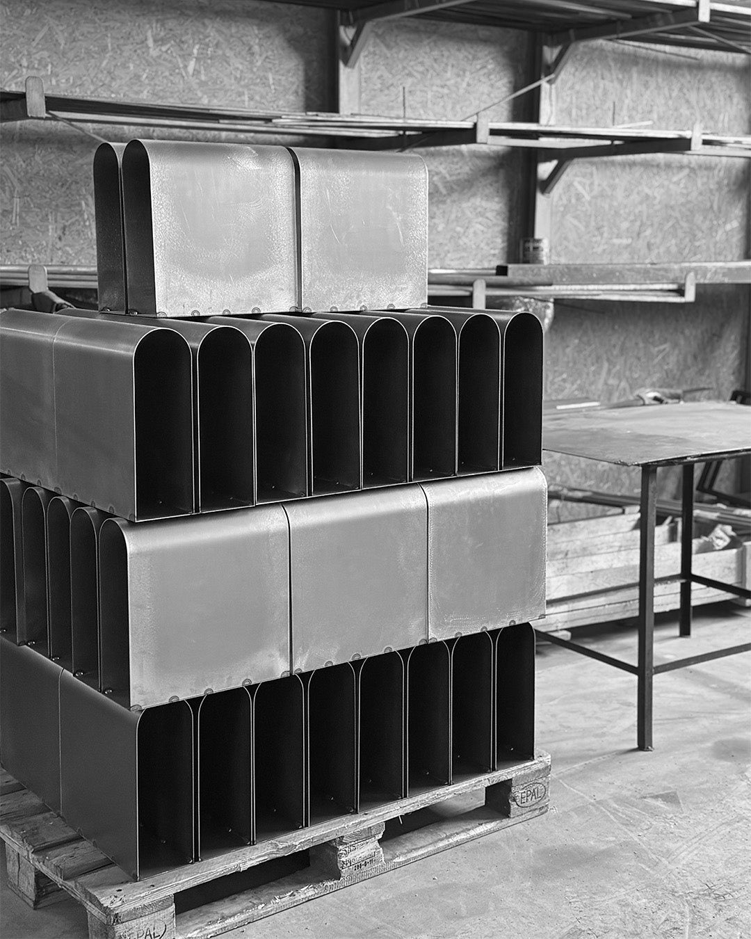 Metal workshop: curved steel bodies of the Curved Side Table stacked on a pallet (black and white).