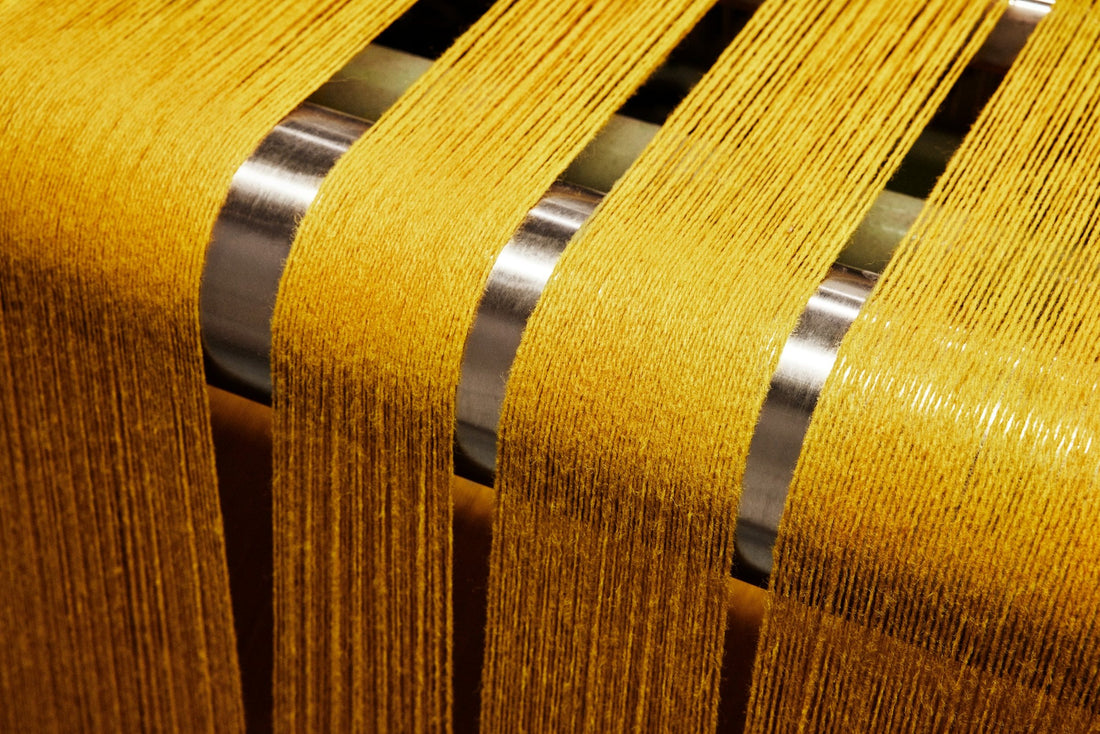 Yellow wool warp threads run over metal guides into the loom, weaving the fabric Sisu at Innvik, Norway.