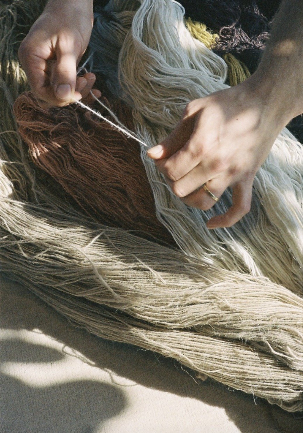 Hands check a strand of yarn among dyed wool skeins.