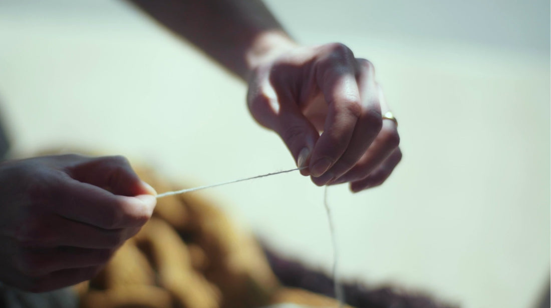 Hands draw out a single strand of wool yarn.