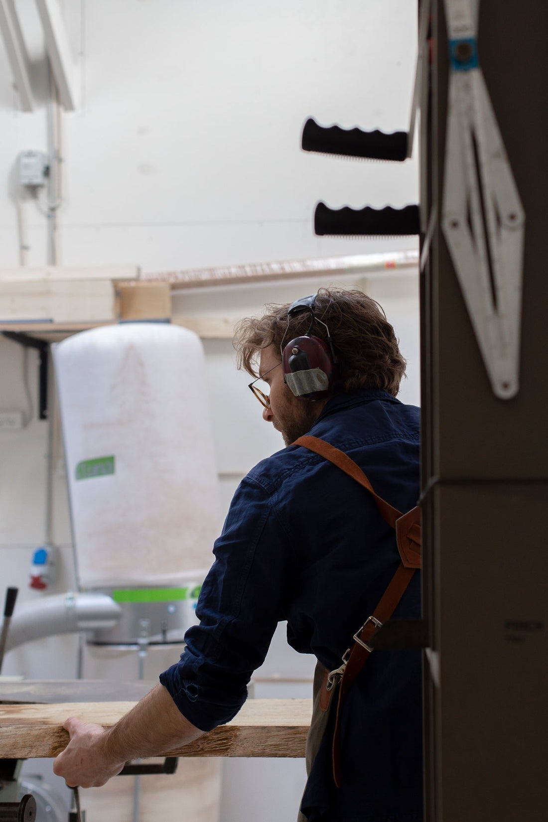 A craftsman with ear protection and a leather apron works on a piece in the workshop.