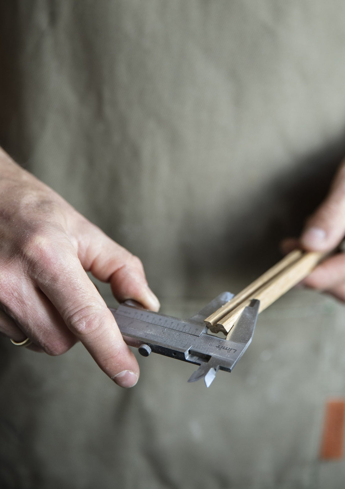 Hands measuring a thin wooden strip with a calliper.