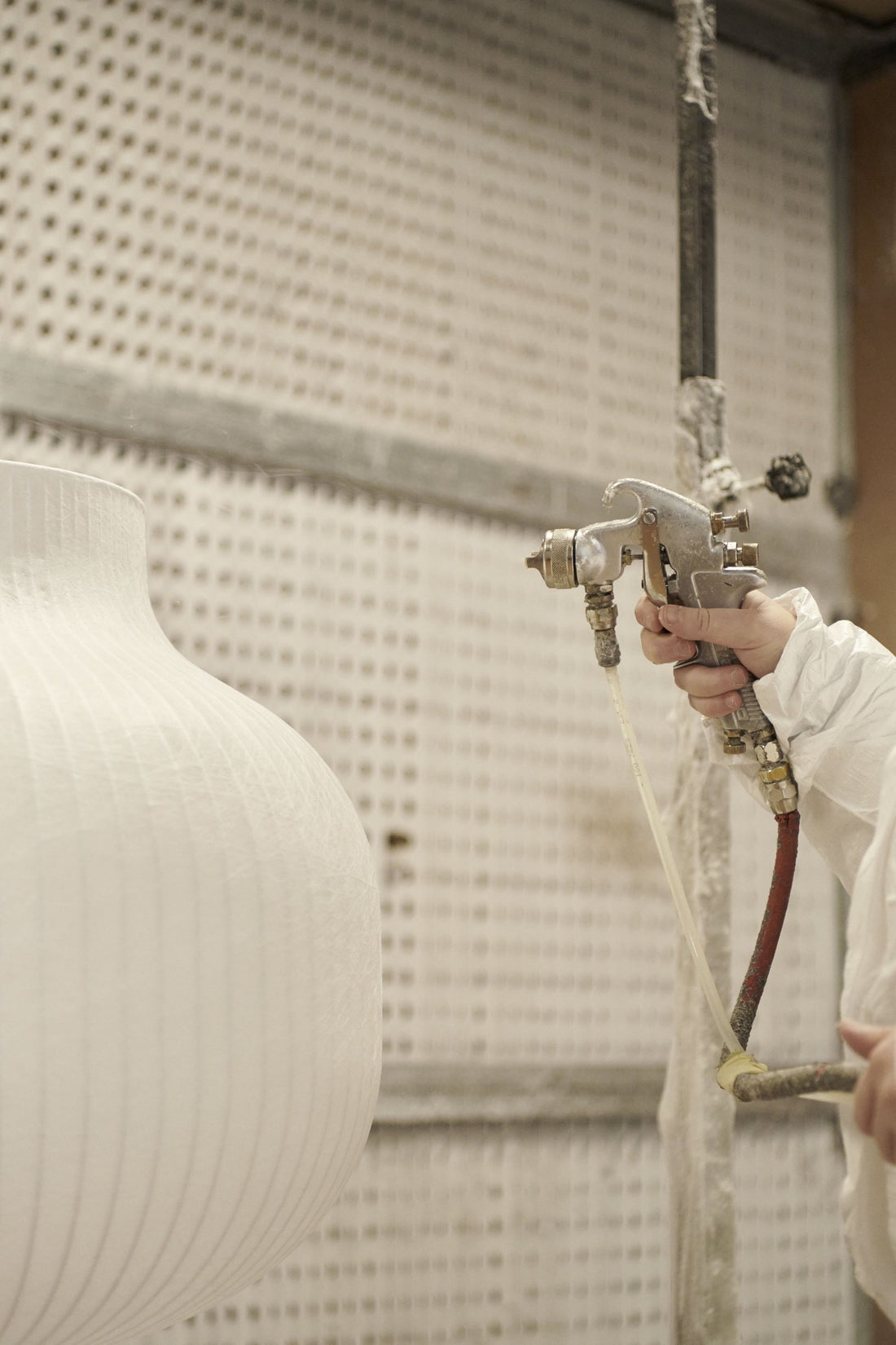 A worker sprays the cocoon material onto the steel frame of a Strand pendant shade (maker in Veneto, Italy).