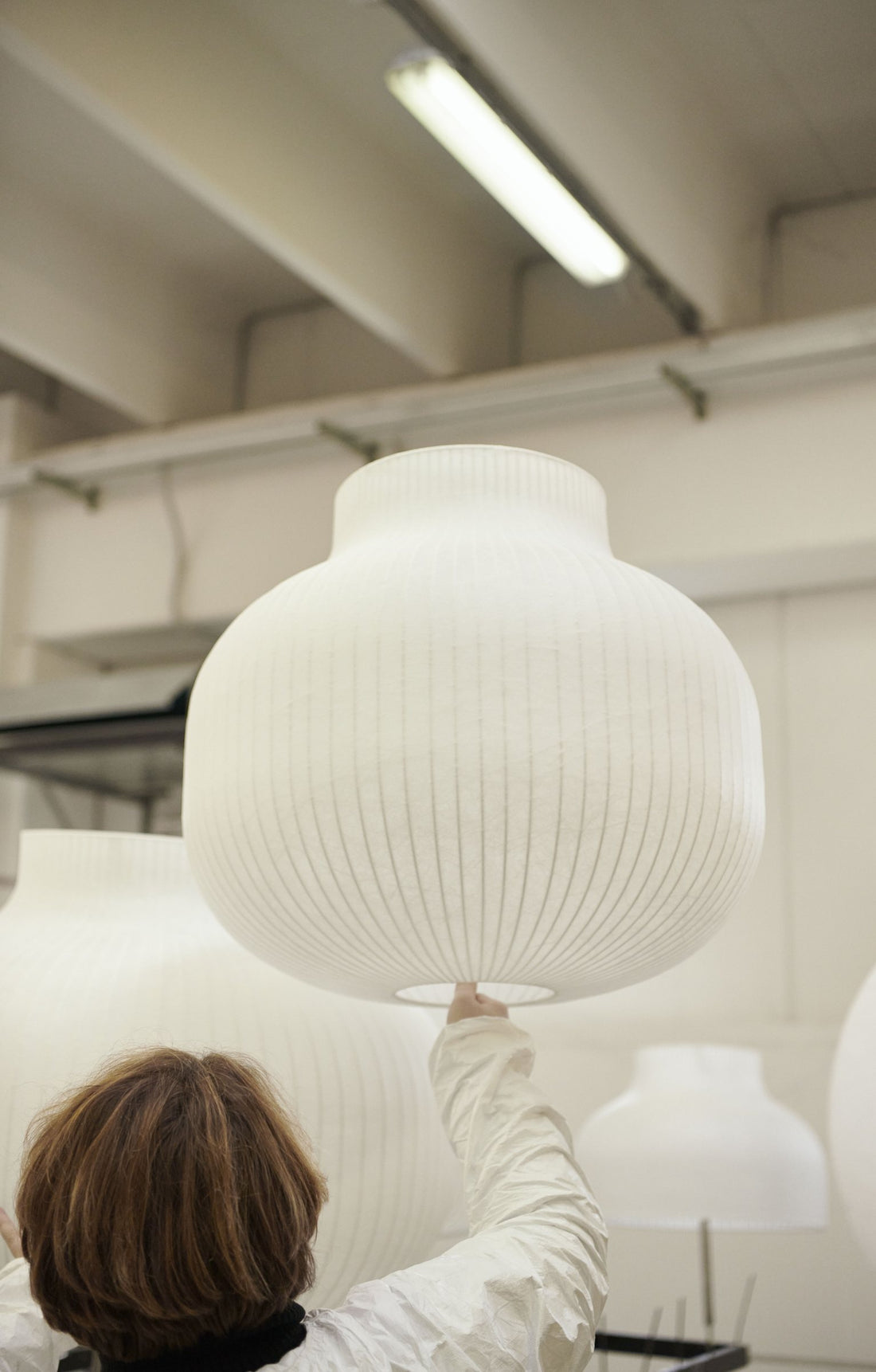 A worker checks and hangs up a finished, coated Strand shade in the production hall.