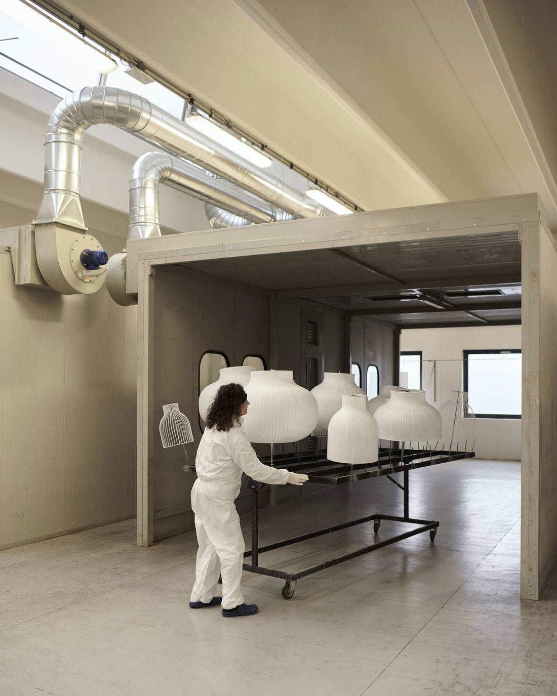 A worker in a protective suit pushes a rack of Strand shades out of the factory's spray booth.