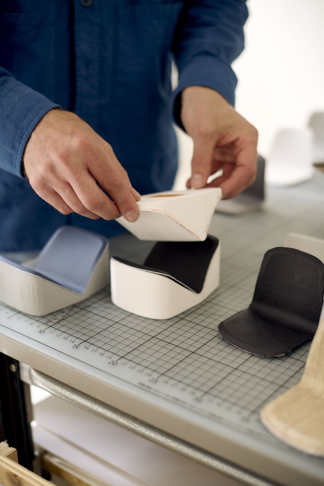 Hands folding a paper model of a chair shell beside seat studies in the designer's studio.