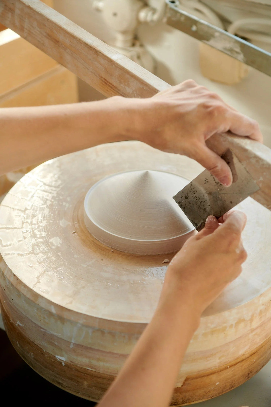 Hands shaping a plaster prototype for a ceramic bowl on a turning wheel in the designers' studio.
