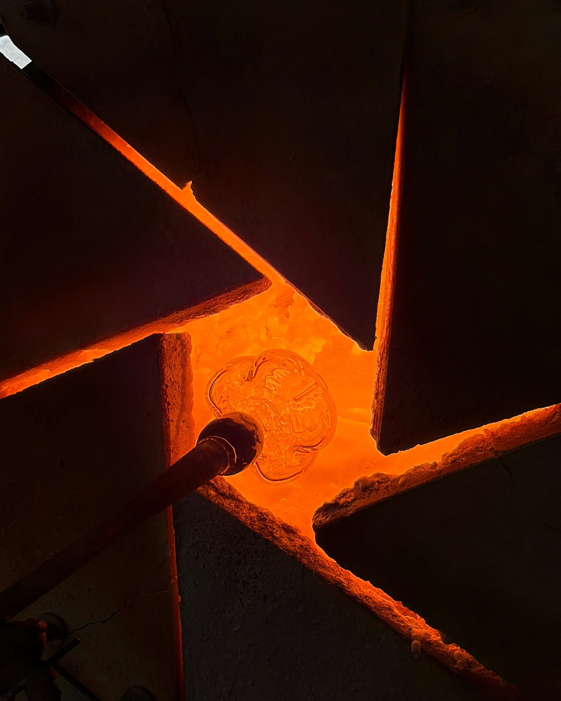 A glass piece on a blowpipe is reheated in the glowing furnace opening.