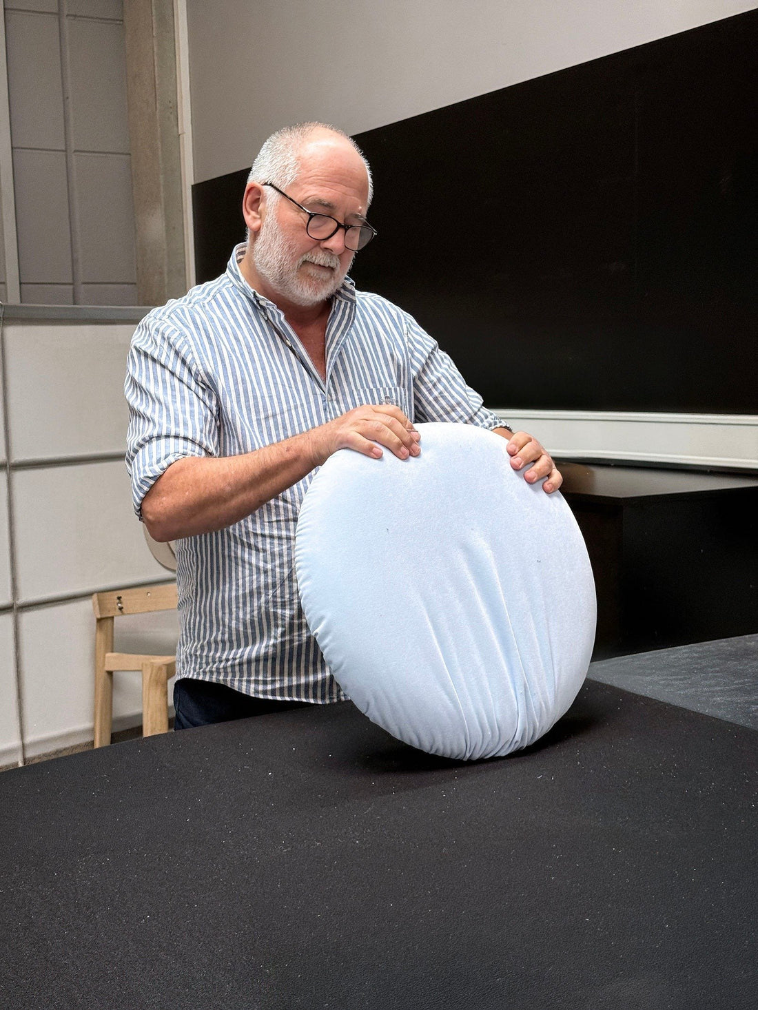 An upholsterer smooths the cover over a round seat cushion for the Linde chair.