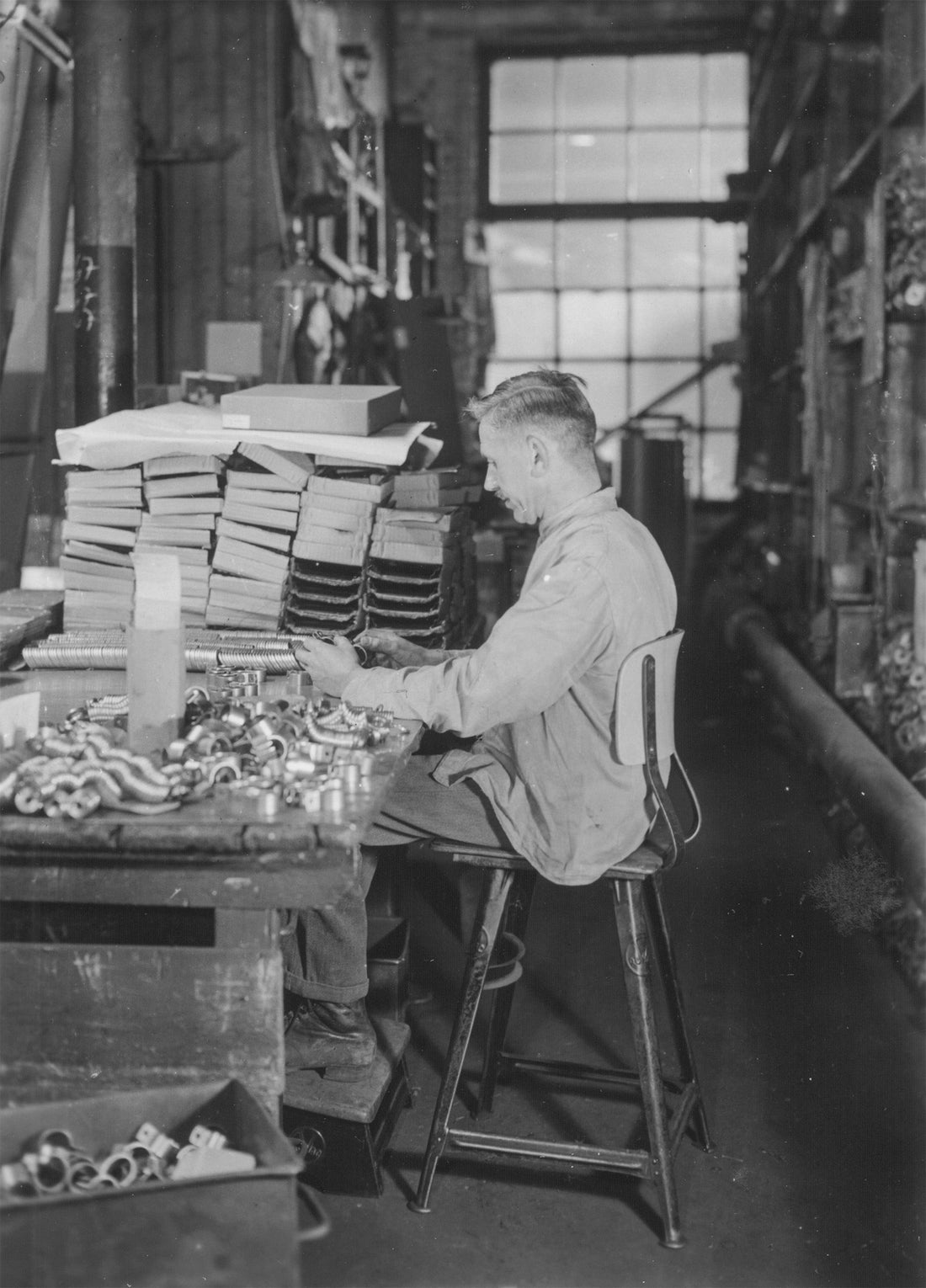 Historic photo, 1938: a worker at Robert Wagner's ROWAC factory in Chemnitz packs metal fittings, seated on a ROWAC stool.