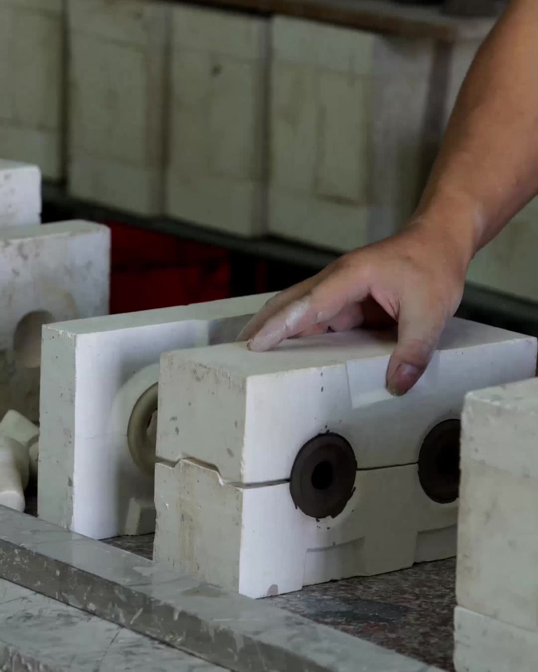 A hand on a two-part plaster casting mould in the ceramics workshop, shelves of moulds behind.